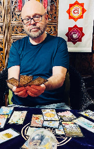 Synchronicity Owner Marcus holding three pulled tarot cards for a reading, in front of a table with tarot cards and crystals.